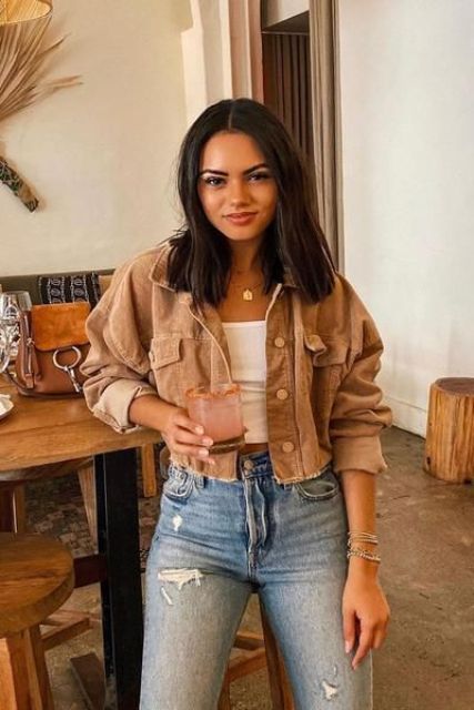 a relaxed look with a white crop top, blue ripped jeans, a tan cropped denim jacket for summer