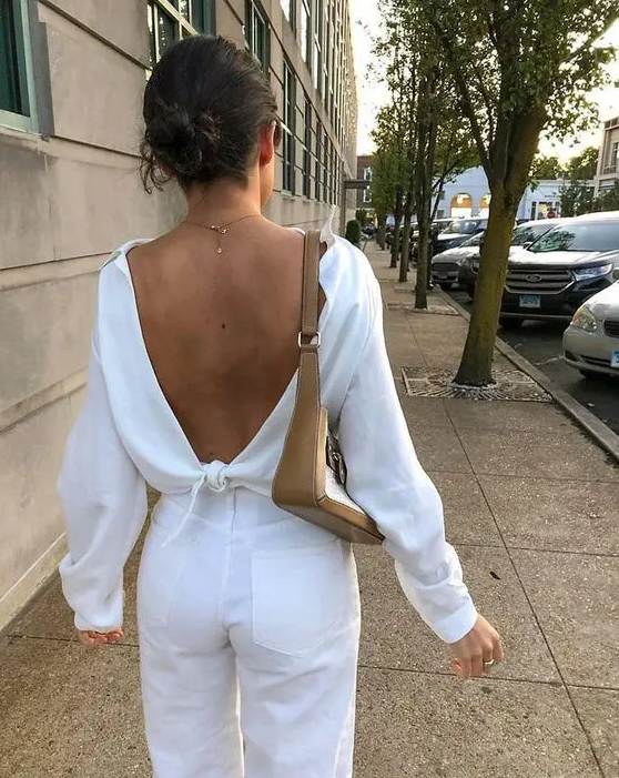 a simple look with white jeans, a white open back top with a tie and long sleeves and a baguette bag