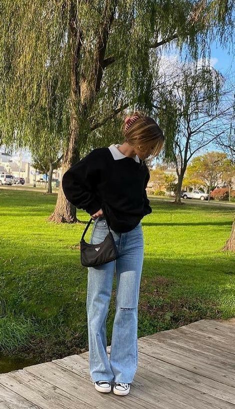a simple outfit with blue flare jeans, a white button down and a black jumper on top, trainers and a black baguette bag