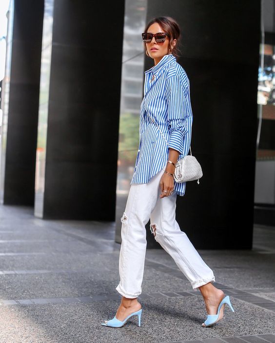 a spring look with an oversized blue strip shirt, white ripped jeans, light blue heeled mules and a white bag