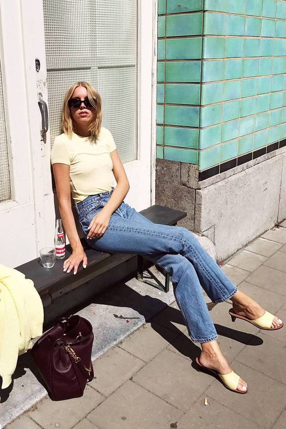 A spring to summer look with a pale yellow t shirt, blue jeans, yellow heeled mules and a burgundy bag