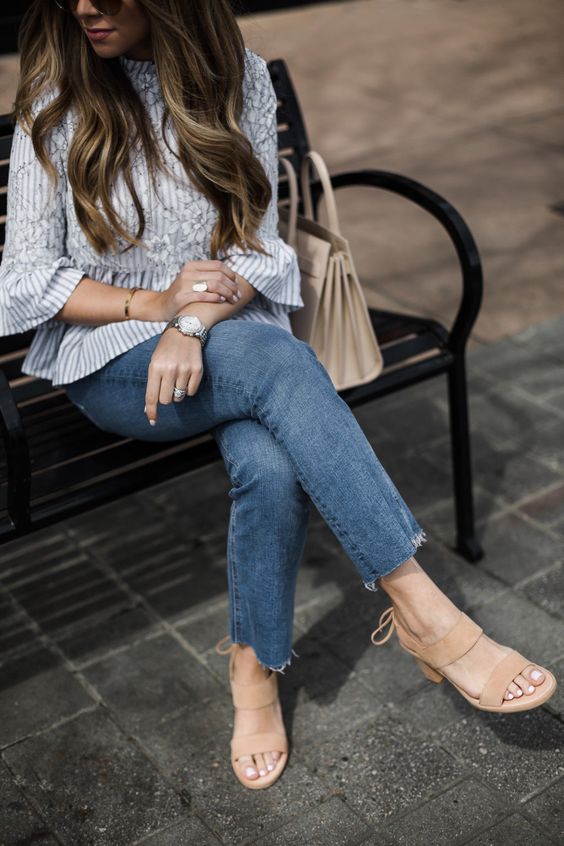 a striped blouse with appliques and ruffle sleeves, blue jeans, tan shoes and a neutral bag