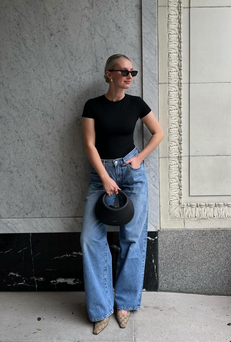 A stylish outfit with a black t shirt, blue wideleg jeans, printed shoes and a small baguette bag, statement earrings and sunglasses