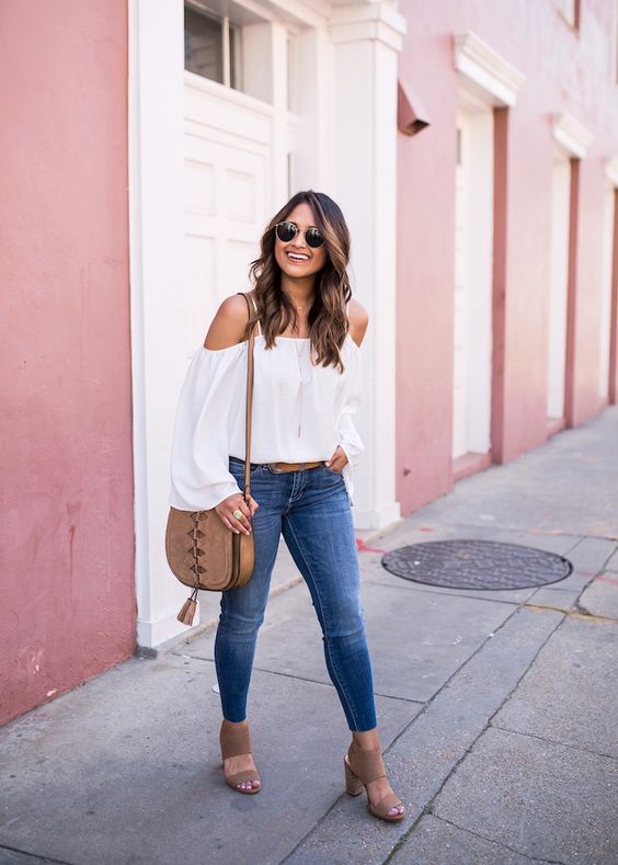 a summer outfit with a white off the shoulder blouse, blue skinnies, tan block heels and a saddle bag
