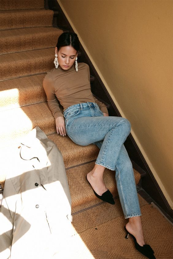 a tan turtleneck, light blue jeans, black velvet heeled mules and statement earrings for a cool spring party look