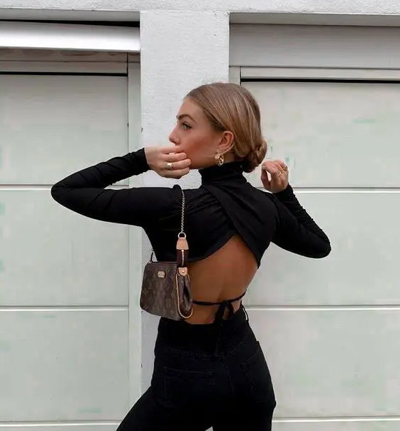 a total black look with a wrapped turtleneck with an open tied back, jeans and a small baguette bag