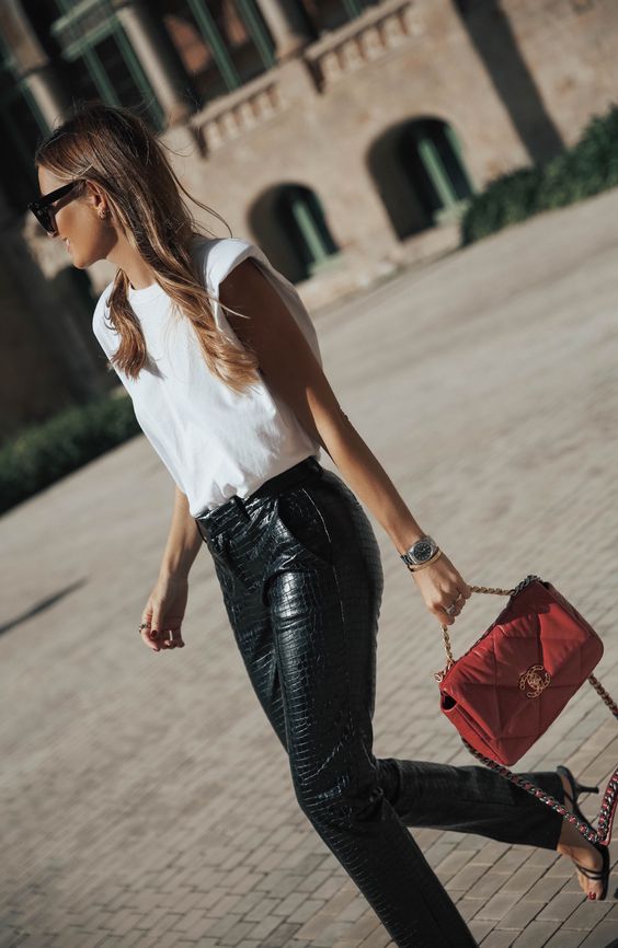 a trendy look with a white padded shoulder top, black reptile leather pants, square toe shoes and a red bag