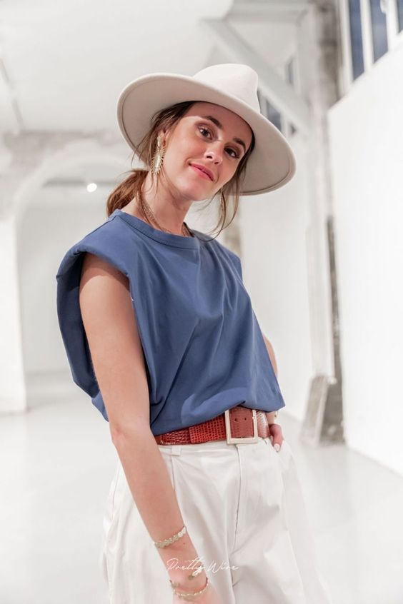 a vacation look with a blue padded shoulder tee, white pants, a red belt, a white hat and statement earrings