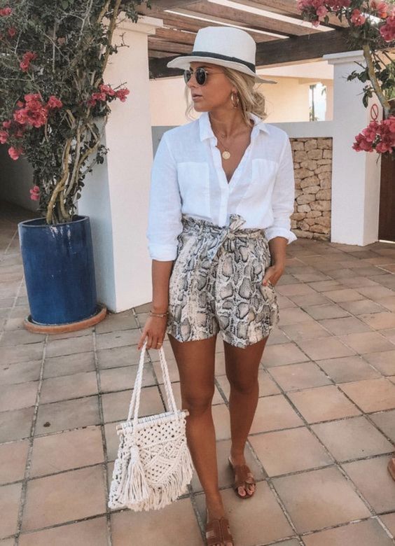 a vacation outfit with a white shirt, snake print shorts, a white hat, brown slippers and a macrame bag