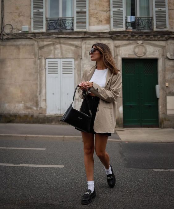 an Old Money outfit with a white top, a black mini skirt, black loafers with white socks, a tan blazer and a black baguette bag