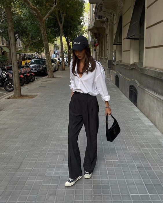 an every day outfit with a white button down, striped trousers, black sneakers, a black cap and a black baguette
