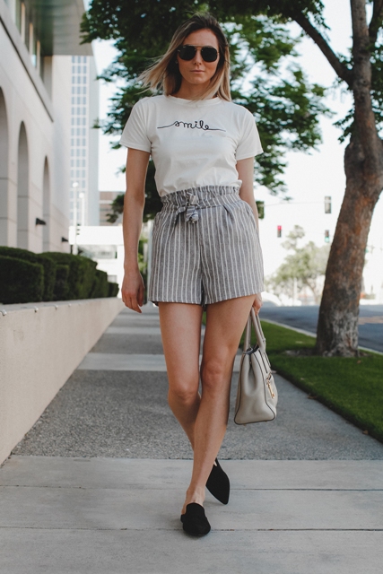 With white labeled t-shirt, gray bag and black flat mules