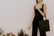 a black fitting jumpsuit with thick straps and cropped pants, black minimalist heels and a black tote