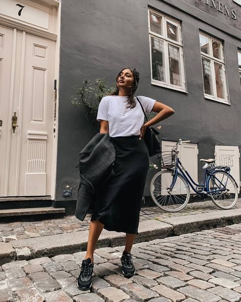 a monochromatic look with a white tee, a black satin midi, black trainers and a black tote