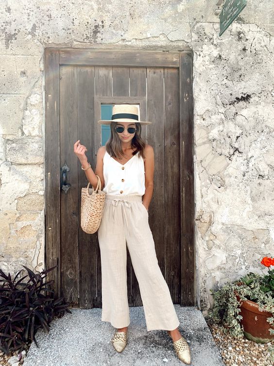 a neutral vacation look with a white button up top, linen pants, gilded flats, a straw hat and a bag
