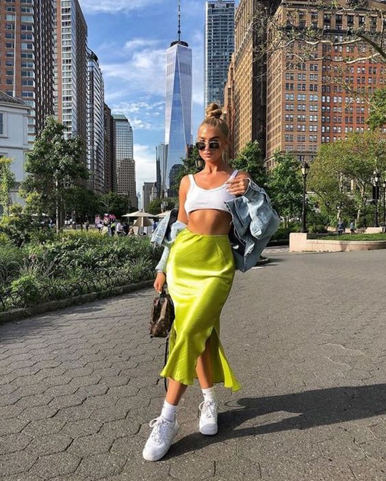 a sporty outfit with a crop top, a neon satin midi, white sneakers and a denim jacket