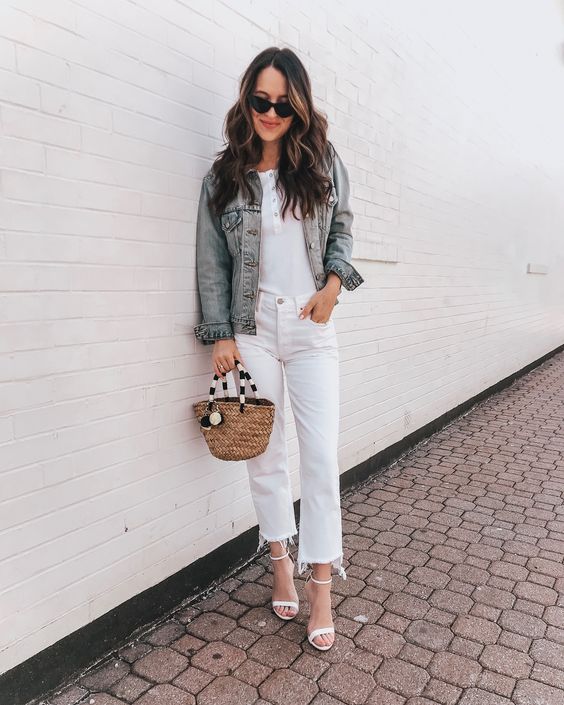 a white button up top, white jeans with a raw hem, white heels, a blue denim jacket and a wicker bag