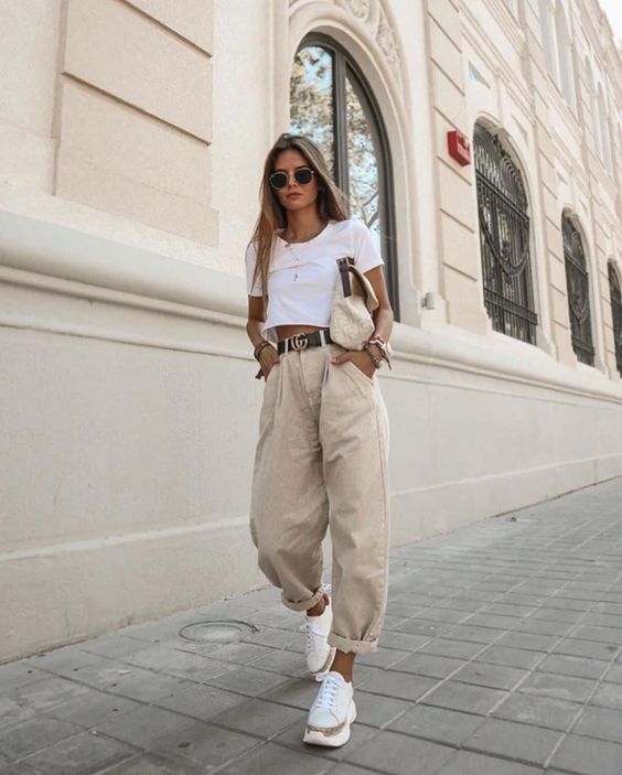 a white crop top, tan baggy jeans, neutral trainers and a fabric bag compose a comfy outfit