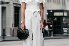 a white off the shoulder striped jumosuit with culottes, black minimalist block heels and a black bag