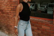 a black halter top, blue high waisted jeans, a large white clutch and statement earrings