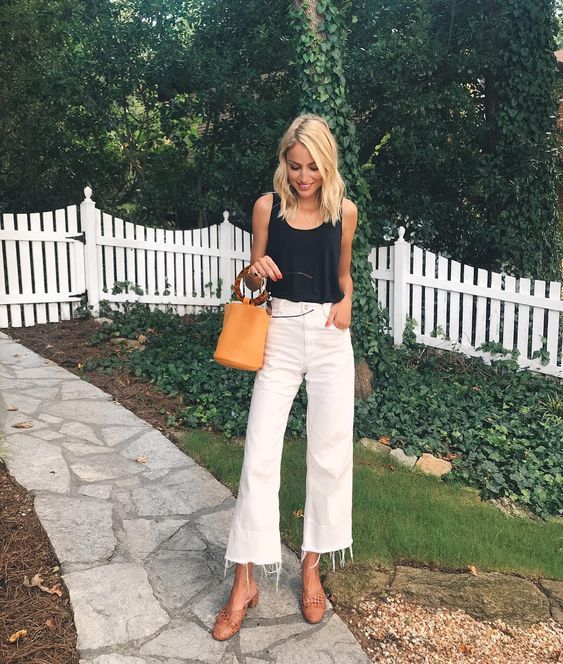 a black top, white raw hem jeans, brown perforated mules and an amber bucket bag on ring handles