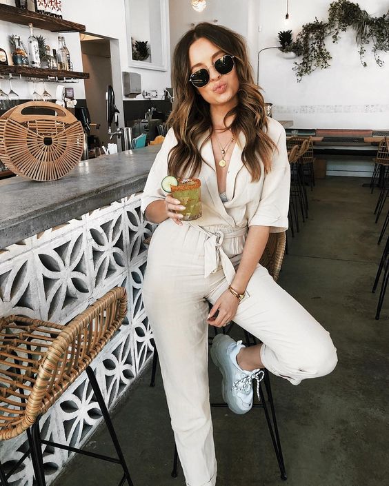 a creamy jumpsuit, white trainers, layered necklaces and a wooden bag for maximal comfort