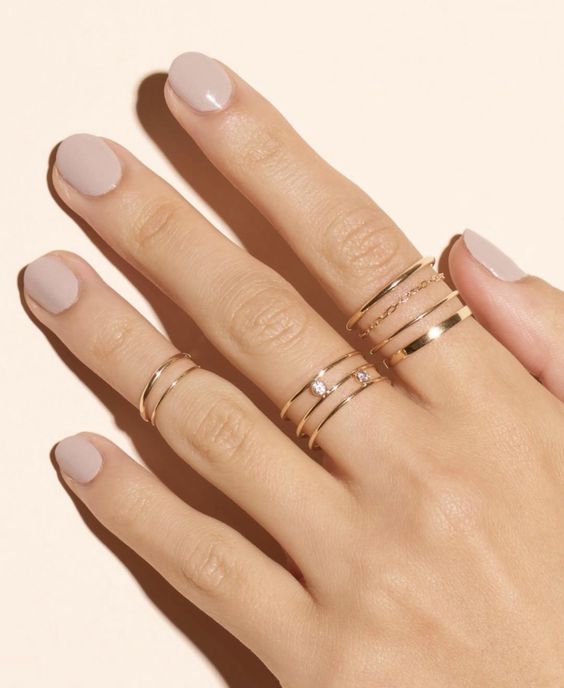 a delicate manicure is highlighted with gold rings with chains and rhinestones and gold midi rings