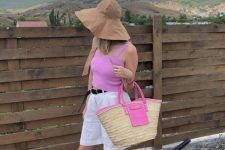 a hot pink crop top, white Bermuda shorts, black flipflops, a bucket hat and a hot pink raffia bag