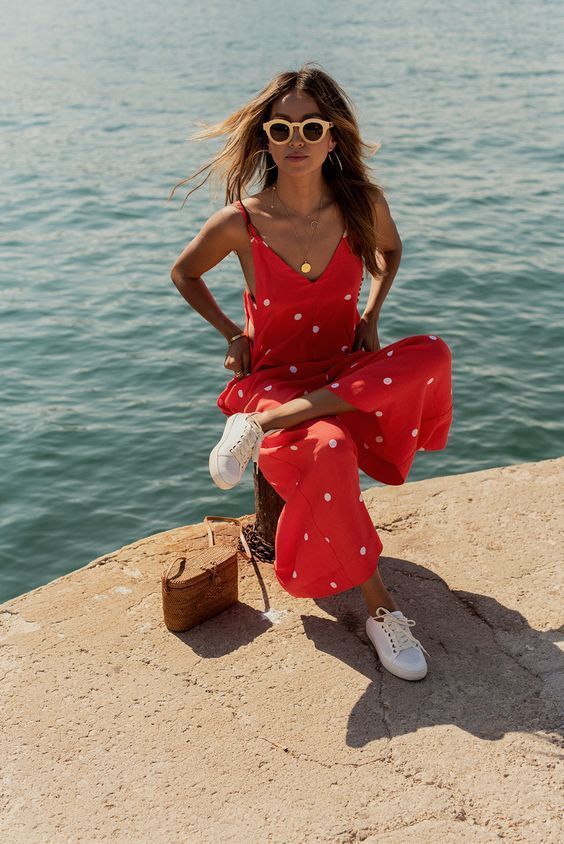 a hot red polka dot jumpsuit with culottes, white sneakers and a small woven bag