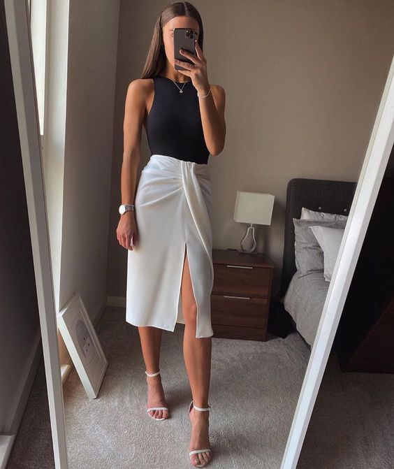 a monochromatic minimalist outfit with a black halter top and a layered wrap midi skirt, white minimalist heels