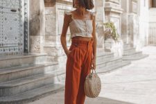 a neutral crop top with ruffle cap sleeves, rust-colored high waisted pants, white espadrilles and a woven bag