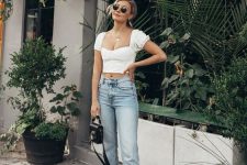 a simple casual look with a white corset crop top with puff sleeves, blue jeans with a raw edge and white slippers plus a small black bag
