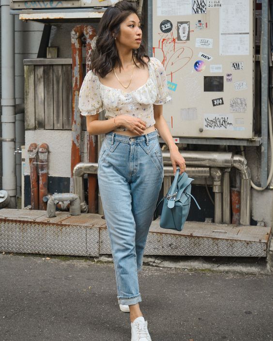 a stylish outfit with blue jeans, a floral crop top with puff sleeves, a powder blue bag and white sneakers