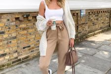 a whiet crop top, tan paper bag pants, white sneakers, a white knit cardgian and a chocolate brown bag