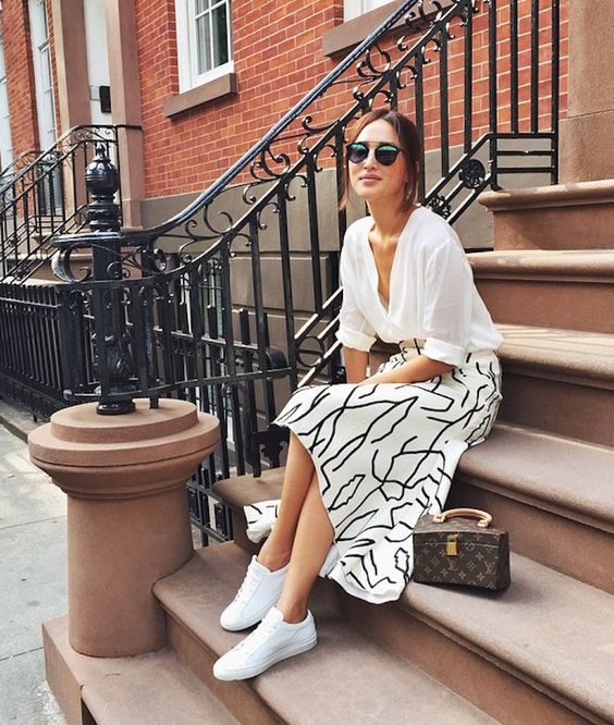 a white shirt, a printed A line midi skirt, white sneakers and a stylish mini top handle bag