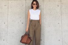a white sleeveless top, olive green pants, black heels and a brown top handle bag of a quirky shape