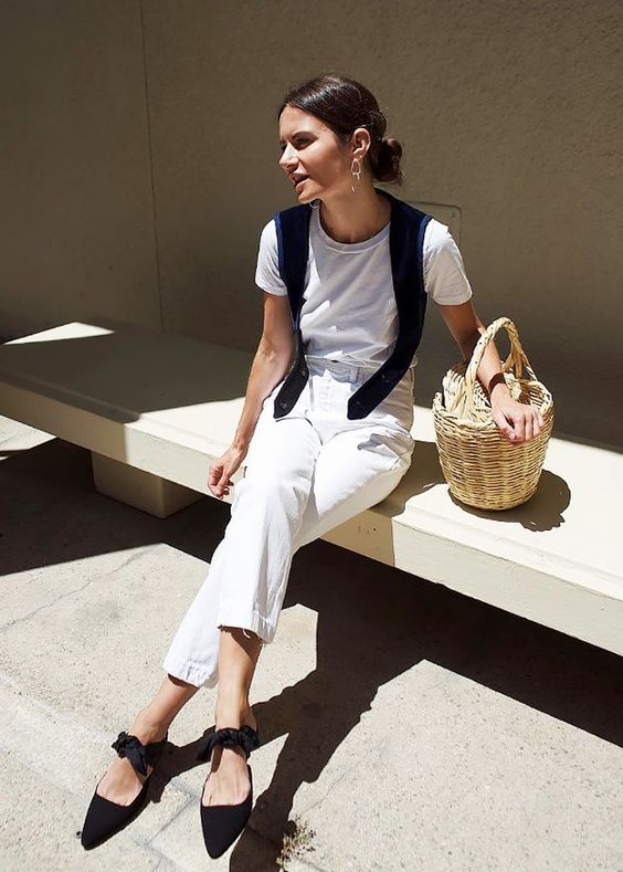a white tee and jeans, black bow mules, a black sweater on the shoulders and a basket bag