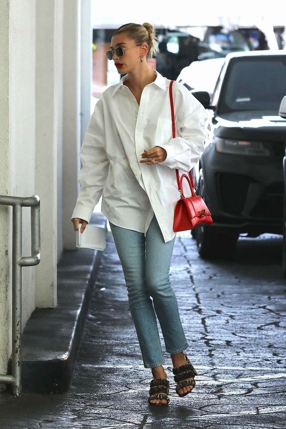 an oversized white shirt, blue jeans, whimsy heels and a small and chic red top handle bag