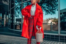a bold outfit with a white knit crop top, plaid pants, silver shoes, an oversized red coat and a bucket bag