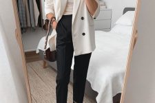 a chic monochromatic outfit with a creamy top and an oversized blazer, black pants and sock boots and a two tone bag