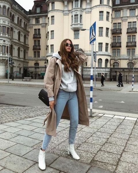 a grey hoodie, blue jeans, white ankle boots, a tan trench and a black bag