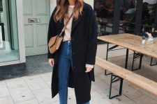 a tan sweater, blue straight leg jeans, a black coat, black booties and a brown crossbody bag