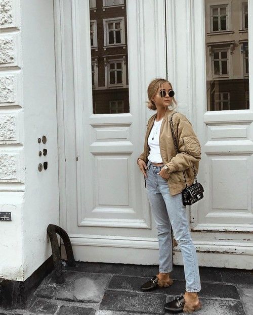a white cropped top, blue jeans, a tan bomber jacket, fur mules and a black crossbody bag