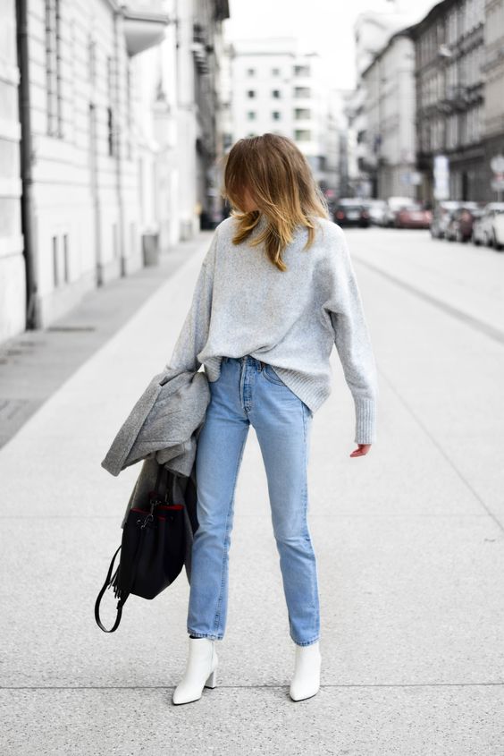 an oversized grey cashmere sweater, blue jeans, white pointed toe boots and a black bag