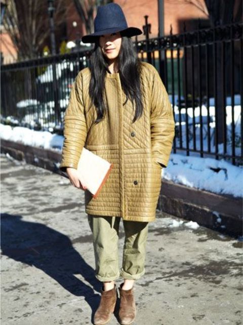 an oversized tan quilted jacket with pockets, green pants, a navy hat, an booties for a fall-infused look