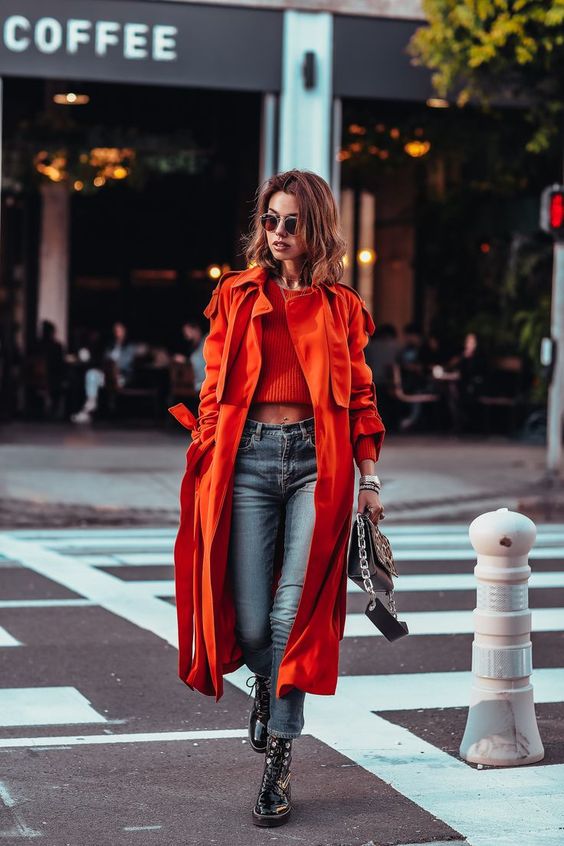 a red crop top, blue jeans, black combat boots, a fiery red midi trench and a black bag