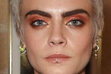 Cara Delevigne rocking several lobe piercings and a lip one done with a shiny rhinestone ring