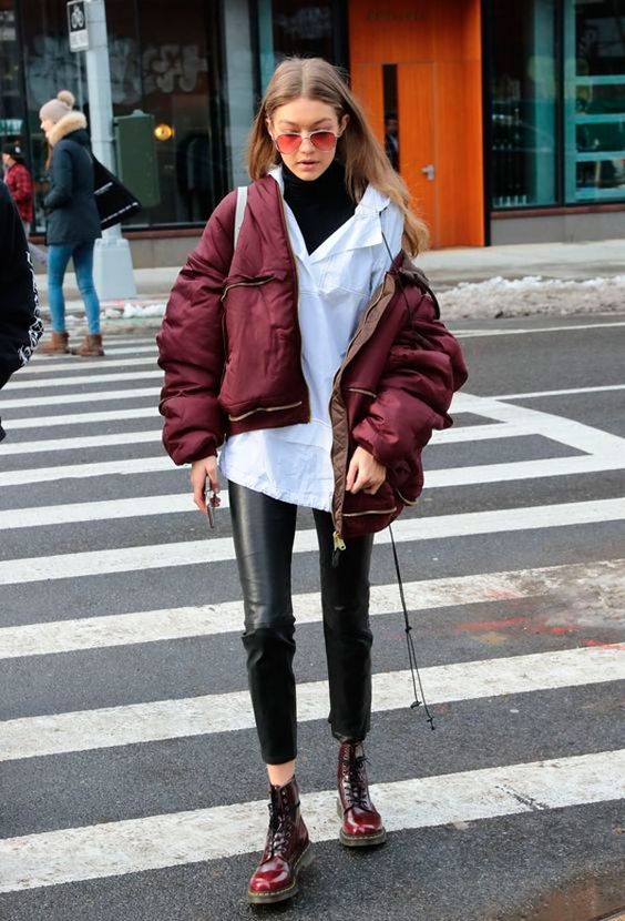 Gigi Hadid wearing a black turtleneck, a white shirt, black leather pants, burgundy boots and a puffer jacket