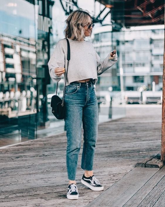 a grey cropped sweatshirt, blue cropped jeans, black sneakers and a black bag with chain