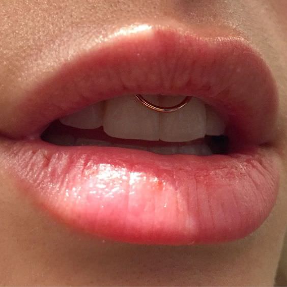 a smiley piercing done with a copper ring jewelry piece and a pink lip for a chic girlish look